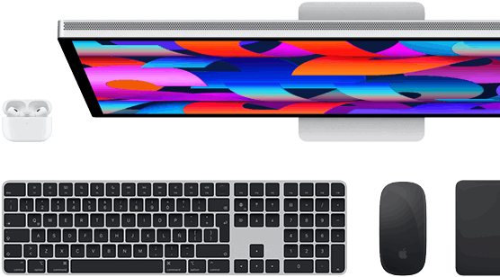 Vista desde arriba de un monitor Studio Display, un Magic Keyboard negro, un Magic Mouse negro, un Magic Trackpad negro y un estuche blanco para los AirPods